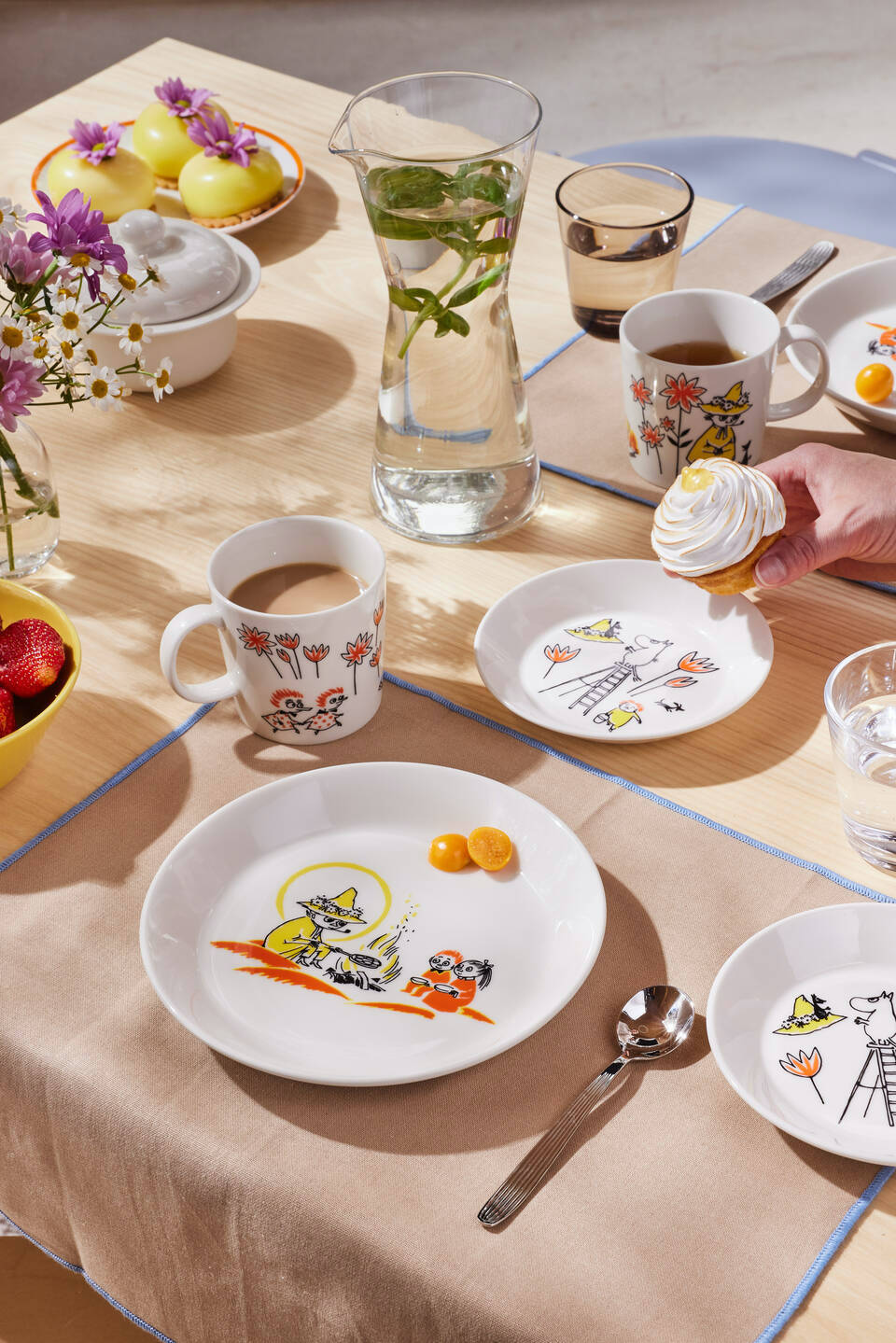 Arabia and Red Cross Moomin dinnerware collection displayed on a laid table with flowers and cupcakes